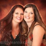 Two smiling women embrace, showcasing warmth and friendship against a vibrant, blurred background. The image conveys a sense of joy and connection.